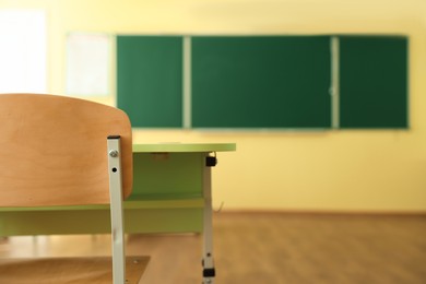 Photo of Desk with chair and green chalkboard in classroom, selective focus