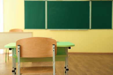 Photo of Desk with chair and green chalkboard in classroom, selective focus