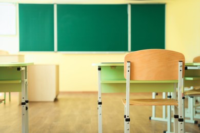 Photo of Desks with chairs and green chalkboard in classroom, selective focus
