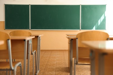 Photo of Desks with chairs and green chalkboard in classroom