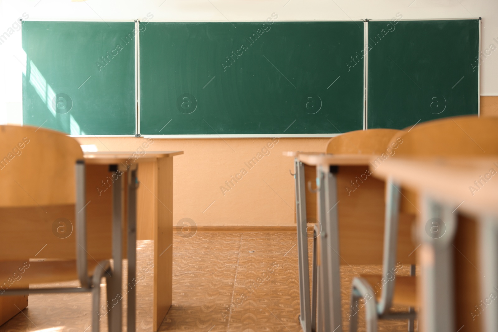 Photo of Desks with chairs and green chalkboard in classroom