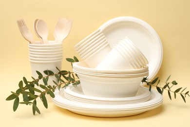 Photo of Disposable tableware and eucalyptus branches on beige background, closeup