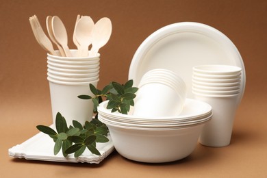 Photo of Disposable tableware and eucalyptus branches on brown background, closeup