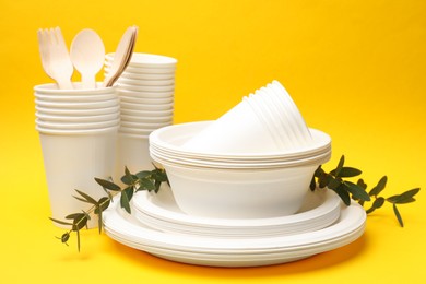 Photo of Disposable tableware and eucalyptus branches on yellow background, closeup