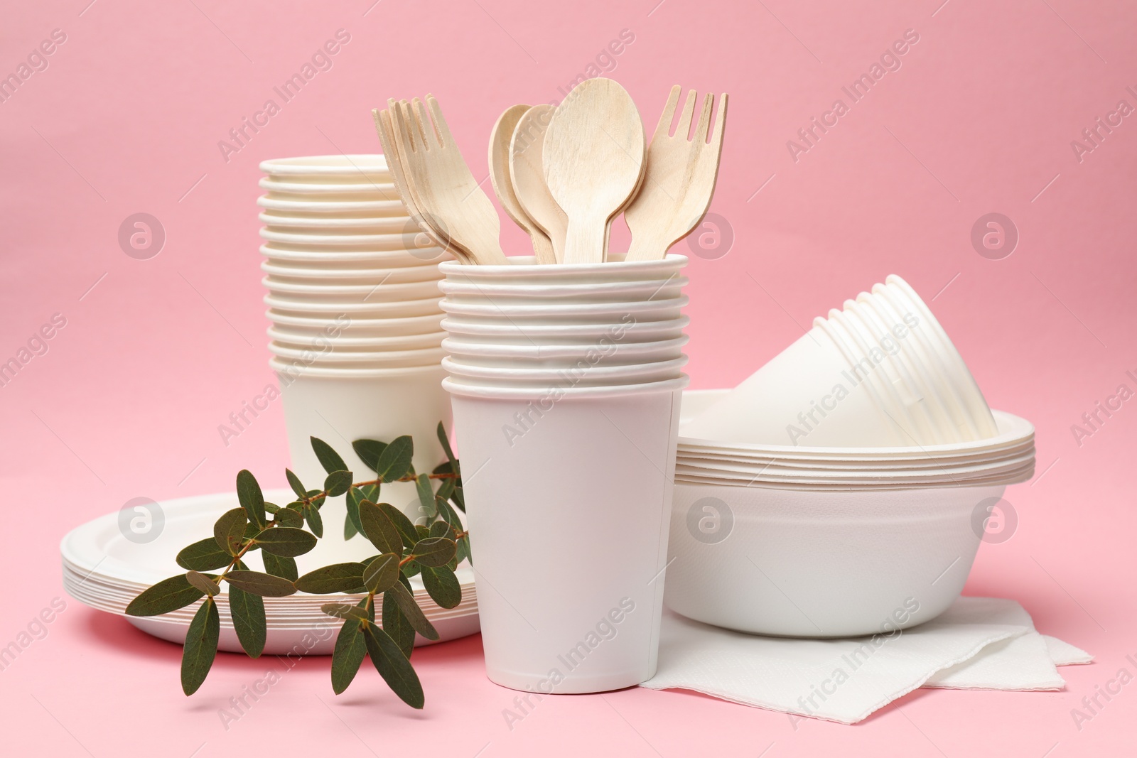 Photo of Disposable tableware and eucalyptus branches on pink background, closeup