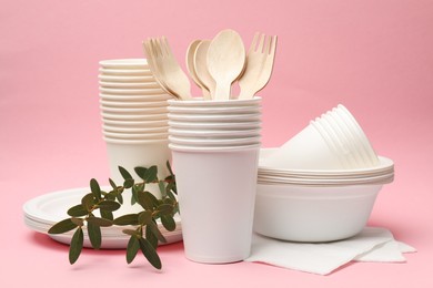 Photo of Disposable tableware and eucalyptus branches on pink background, closeup