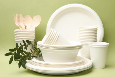 Photo of Disposable tableware and eucalyptus branches on green background, closeup