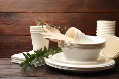 Photo of Disposable tableware and eucalyptus branches on wooden table, closeup