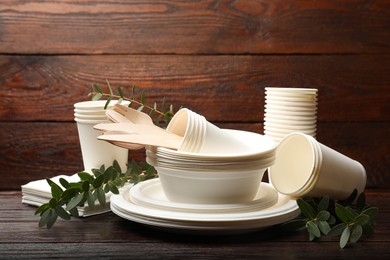 Photo of Disposable tableware and eucalyptus branches on wooden table, closeup