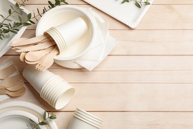 Photo of Set of disposable tableware and eucalyptus branches on light wooden table, flat lay. Space for text