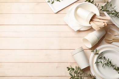 Photo of Set of disposable tableware and eucalyptus branches on light wooden table, flat lay. Space for text