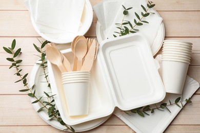 Photo of Set of disposable tableware and eucalyptus branches on light wooden table, flat lay