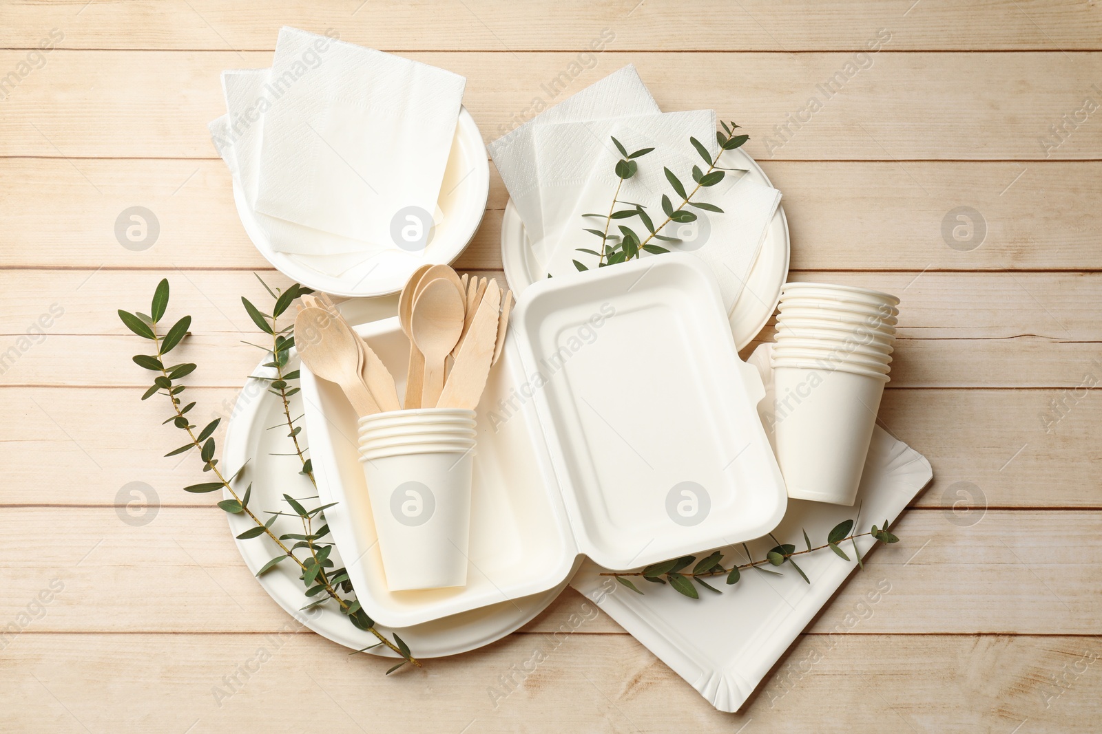 Photo of Set of disposable tableware and eucalyptus branches on light wooden table, flat lay