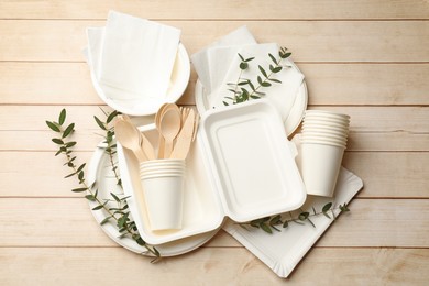 Photo of Set of disposable tableware and eucalyptus branches on light wooden table, flat lay