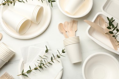 Photo of Set of disposable tableware and eucalyptus branches on white table, flat lay