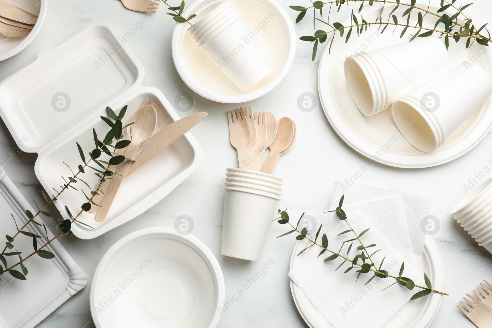 Photo of Set of disposable tableware and eucalyptus branches on white table, flat lay