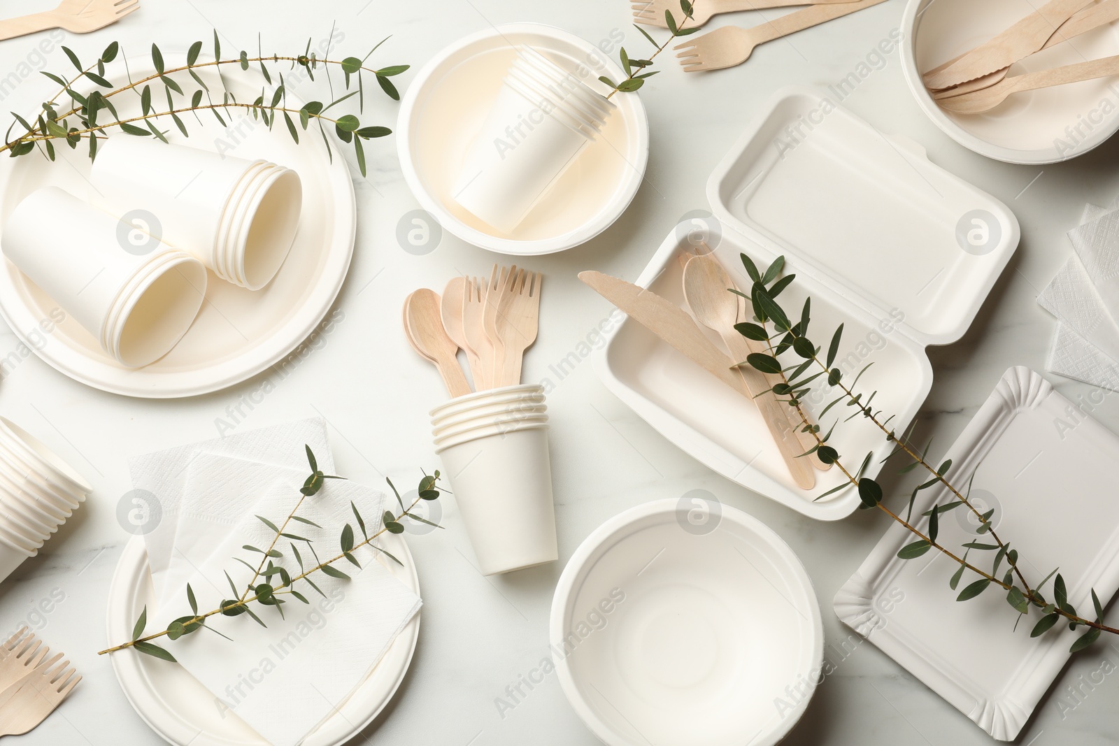 Photo of Set of disposable tableware and eucalyptus branches on white table, flat lay