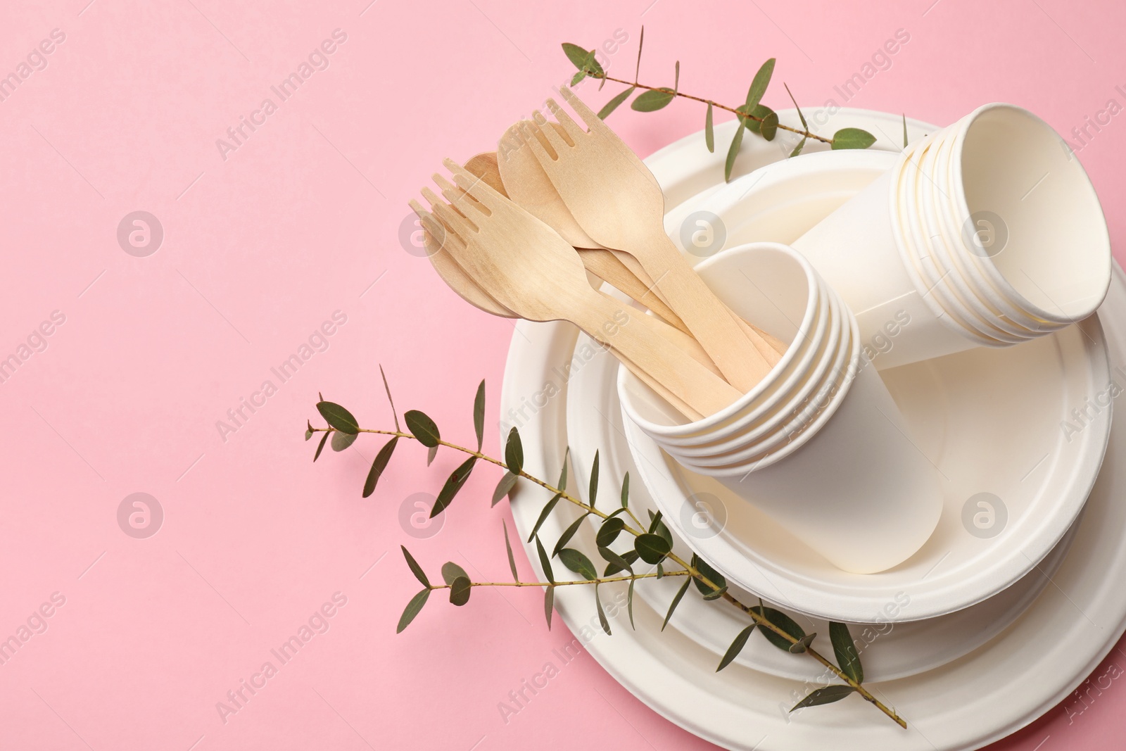 Photo of Set of disposable tableware and eucalyptus branches on pink background, top view. Space for text