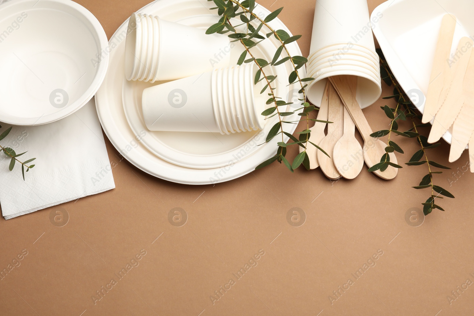 Photo of Set of disposable tableware and eucalyptus branches on brown background, flat lay. Space for text