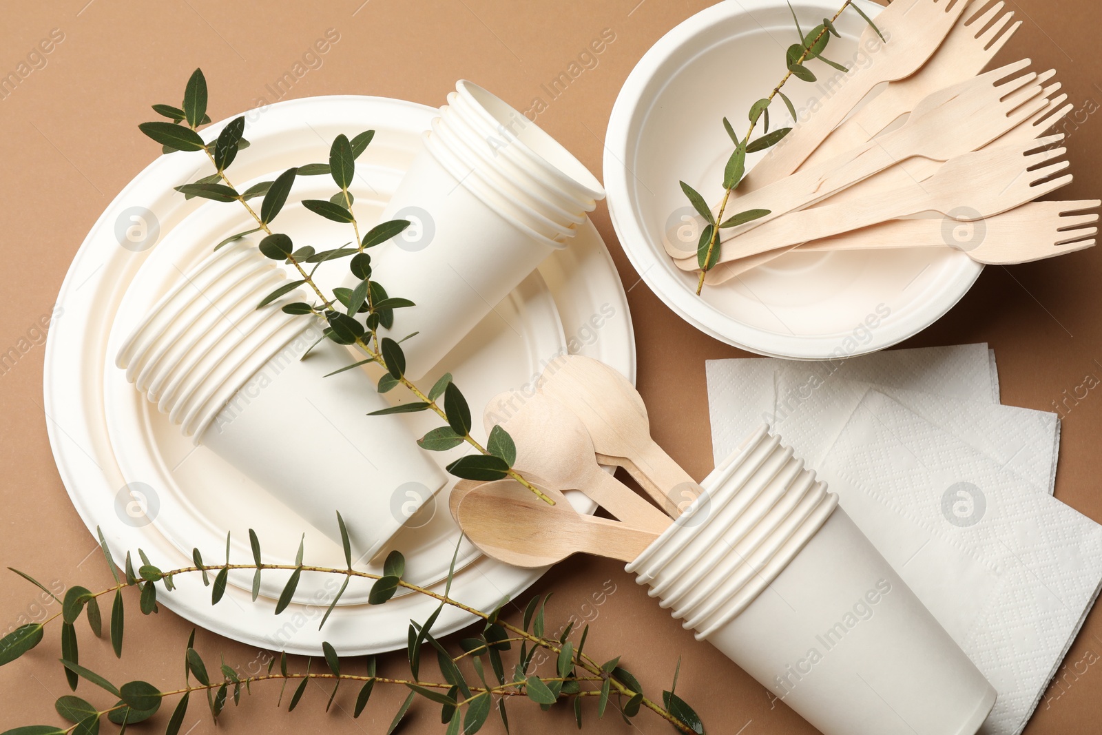 Photo of Set of disposable tableware and eucalyptus branches on brown background, flat lay