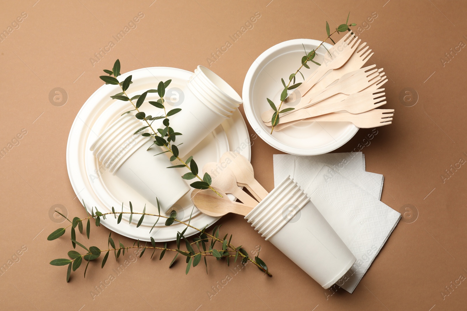 Photo of Set of disposable tableware and eucalyptus branches on brown background, flat lay
