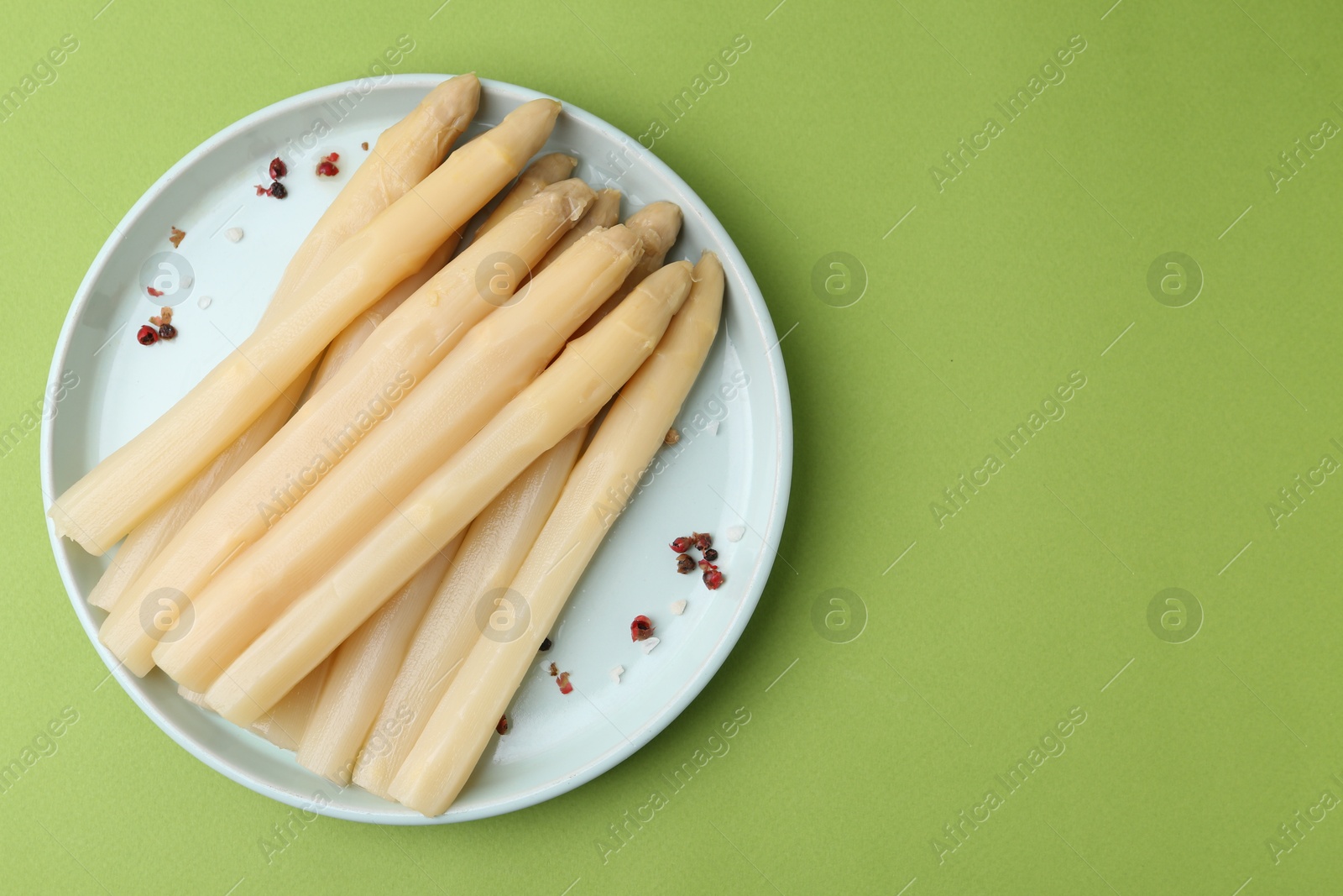 Photo of Pickled asparagus spears with spices on green table, top view. Space for text