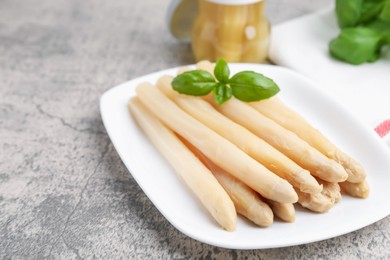 Photo of Pickled asparagus spears with basil on grey table, closeup