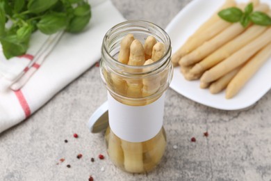 Photo of Pickled asparagus, spices and basil on light grey table, closeup