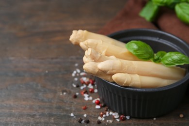 Photo of Pickled asparagus with basil and spices on wooden table, closeup. Space for text