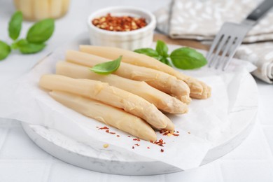 Photo of Pickled asparagus spears with spices and basil on white table, closeup