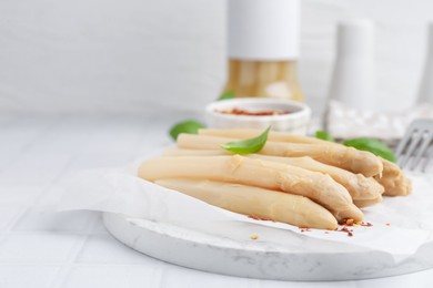 Photo of Pickled asparagus spears with spices and basil on white table, closeup