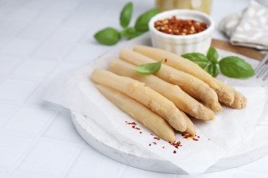 Photo of Pickled asparagus spears with spices and basil on white table, closeup
