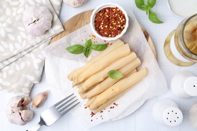 Photo of Pickled asparagus spears served on white tiled table, flat lay