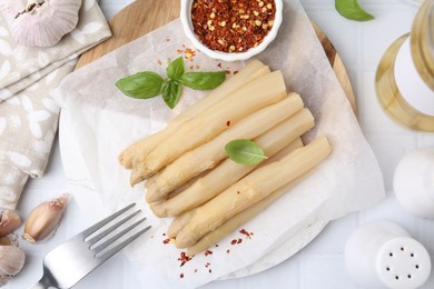 Photo of Pickled asparagus spears served on white tiled table, flat lay