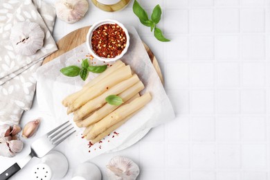 Photo of Pickled asparagus spears served on white tiled table, flat lay. Space for text