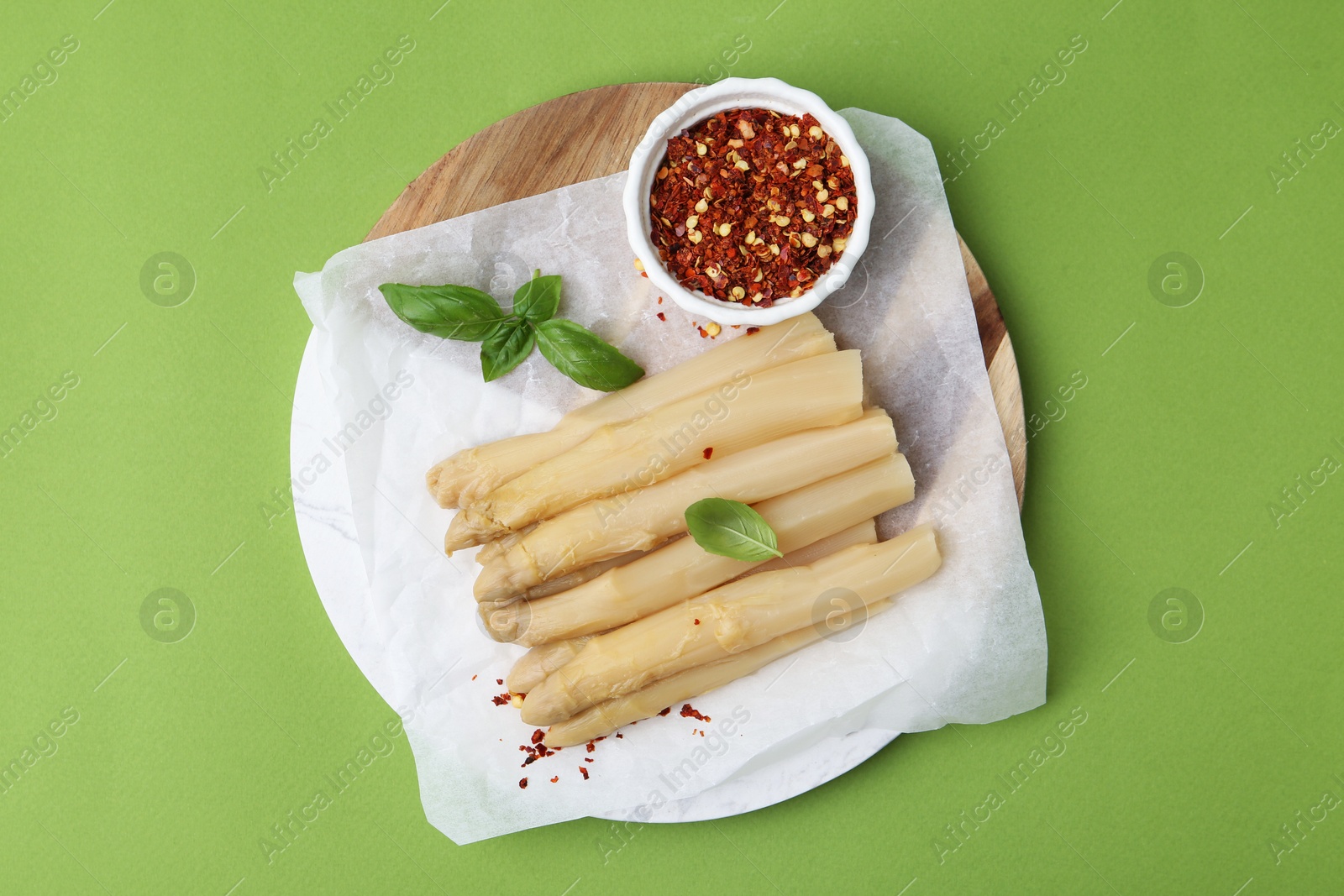 Photo of Pickled asparagus spears with spices and basil on green table, top view