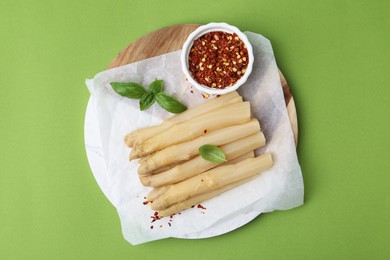 Photo of Pickled asparagus spears with spices and basil on green table, top view