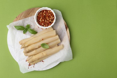 Photo of Pickled asparagus spears with spices and basil on green table, top view. Space for text