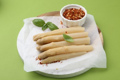 Photo of Pickled asparagus spears with spices and basil on green table, closeup