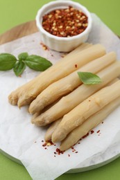 Photo of Pickled asparagus spears with spices and basil on green table, closeup