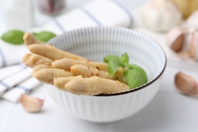 Photo of Pickled asparagus spears with spices in bowl on white table, closeup