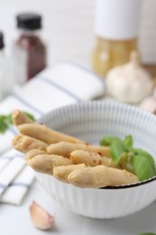 Photo of Pickled asparagus spears with spices in bowl on white table, closeup
