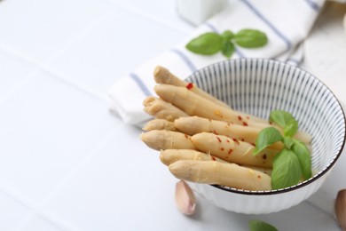 Photo of Pickled asparagus with spices, basil and garlic on white tiled table, closeup. Space for text