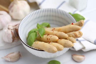 Photo of Pickled asparagus with spices, basil and garlic on white table, closeup