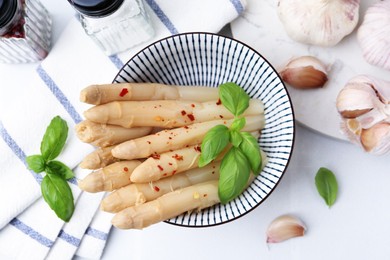 Photo of Pickled asparagus with spices, basil and garlic on white table, flat lay