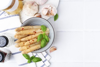 Photo of Pickled asparagus with spices, basil and garlic on white tiled table, flat lay. Space for text