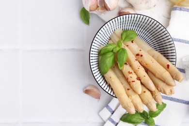 Photo of Pickled asparagus with spices, basil and garlic on white tiled table, flat lay. Space for text