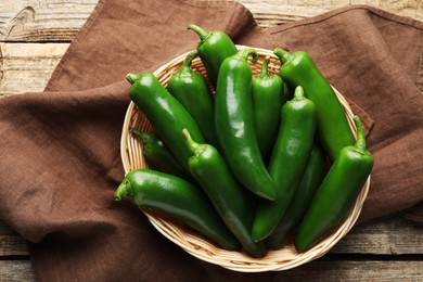 Photo of Ripe green jalapeno peppers in basket and towel on wooden table, top view