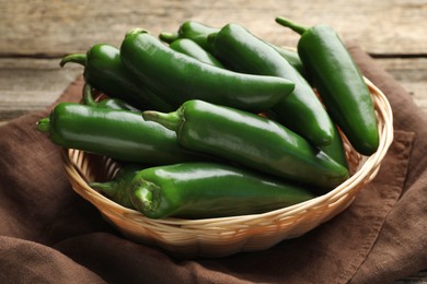 Photo of Ripe green jalapeno peppers in basket and towel on wooden table, closeup