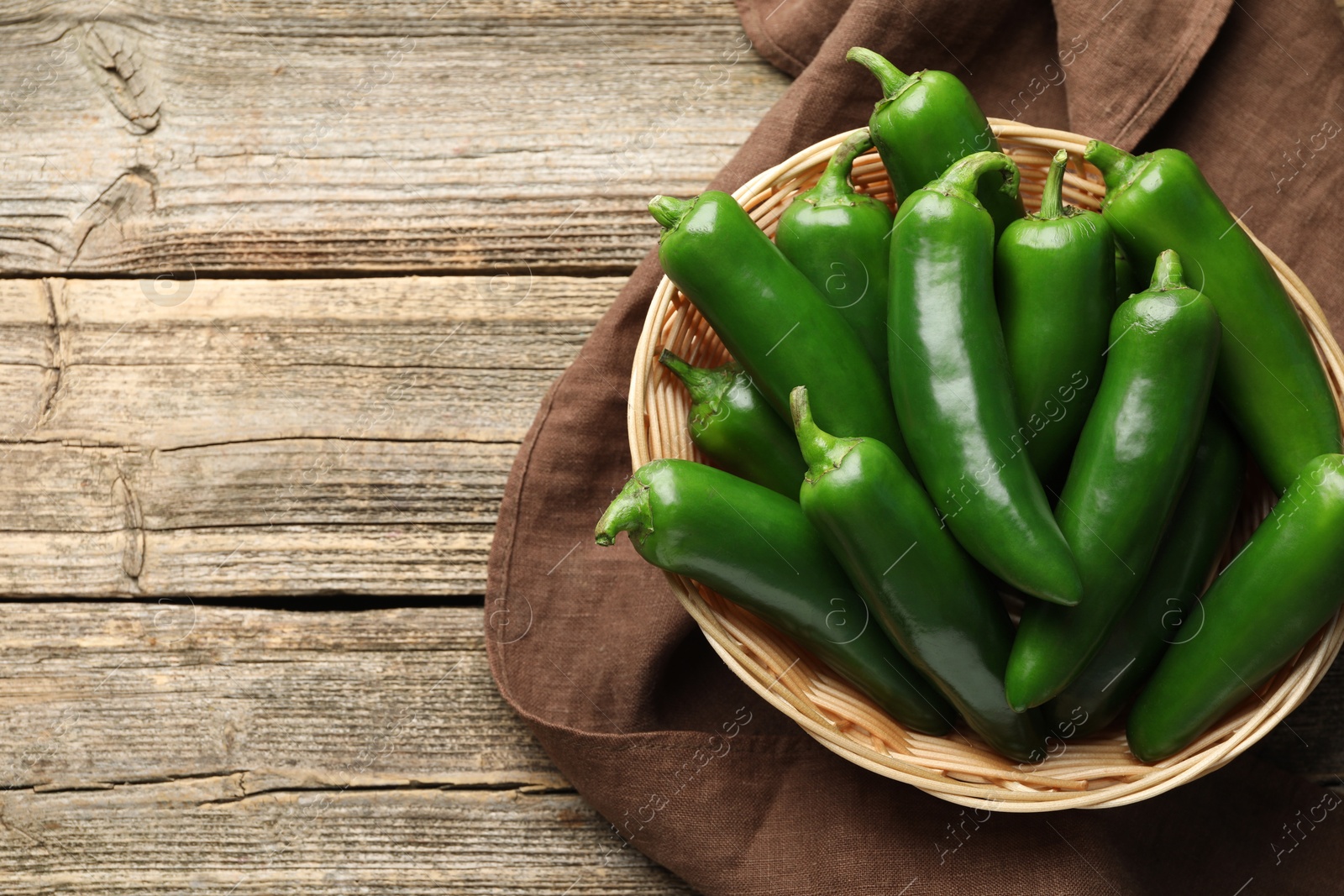 Photo of Ripe green jalapeno peppers in basket and towel on wooden table, top view. Space for text